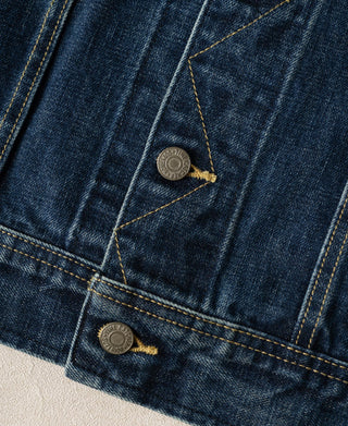 Indigo denim jacket close-up of flap pockets with brass-toned buttons and contrast yellow stitching