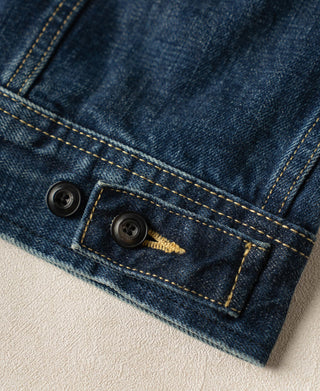 Indigo denim jacket cuff and hem close-up with dark buttons and contrast yellow stitching