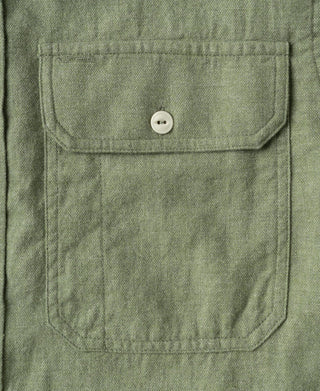 Sage green work shirt chest pocket detail with flap and round white button.