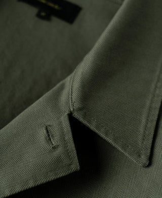 Olive herringbone field jacket cuff with dark button and folded edge.