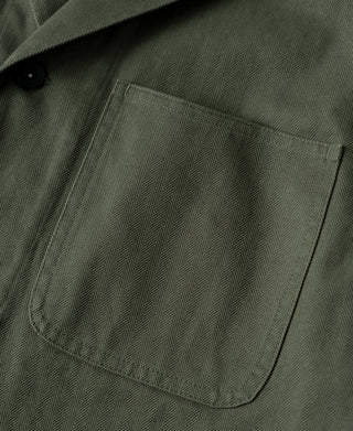 Olive field jacket chest pocket with curved flap and dark button.