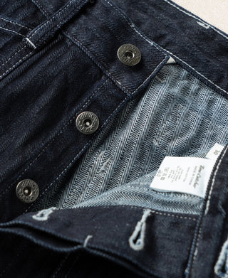 Indigo denim pants with metal buttons, chevron lining at waistband, and label tag