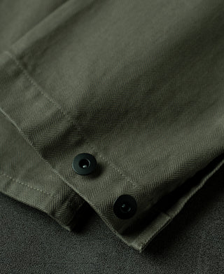 Olive herringbone jacket cuff with dark snap button and stitched seam.