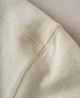 Close-up of cream cotton henley side seam and ribbed trim edge