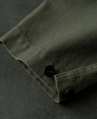 Olive herringbone jacket sleeve cuff with dark button and seam stitching.