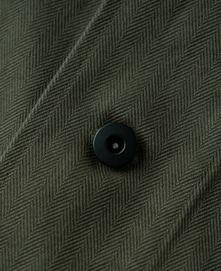 Olive herringbone jacket button on fabric panel with visible stitching.