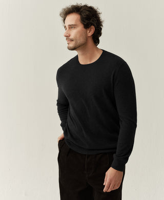 Side view of a man wearing a black merino wool crewneck sweater with a relaxed elegant fit