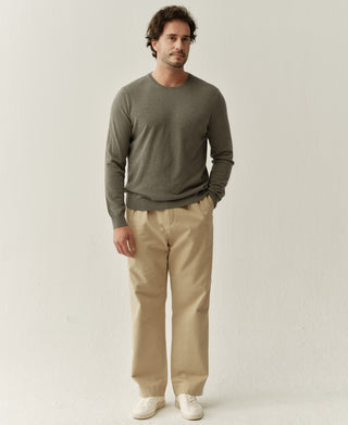 Full body view of a man wearing a grayish green merino wool crewneck sweater styled with casual trousers