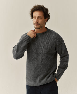 Model wearing a gray wool sweater and touching its mock neck collar