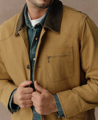 Khaki field jacket detail with zippered chest pocket, dark collar, and button front.